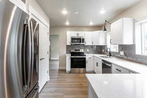Kitchen featuring stainless steel appliances, white cabinetry, decorative backsplash, decorative light fixtures, and light wood-type flooring