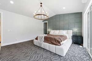 Carpeted bedroom featuring lofted ceiling, recessed lighting, a chandelier, and an accent wall
