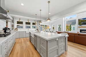 Kitchen featuring glass insert cabinets, decorative light fixtures, gray cabinetry, wall chimney range hood, and open floor plan