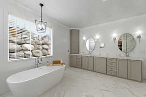 Bathroom featuring double vanity, a soaking tub, light marble finish floors, a textured ceiling, and a chandelier