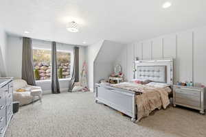 Bedroom with light carpet, lofted ceiling, a textured ceiling, and a decorative wall