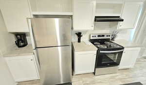 Kitchen featuring stainless steel appliances, light countertops, white cabinetry, range hood, and backsplash