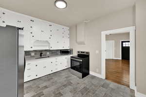 Kitchen with stainless steel appliances, light countertops, white cabinets, and backsplash