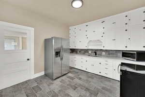 Kitchen featuring appliances with stainless steel finishes, white cabinets, backsplash, and light stone countertops