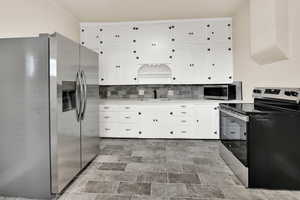 Kitchen with stainless steel appliances, white cabinets, tasteful backsplash, and light stone countertops