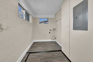 Washroom with electric panel, wood finished floors, concrete block wall, and hookup for a washing machine