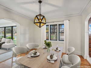 Dining room with arched walkways, wood finished floors, crown molding, and a chandelier