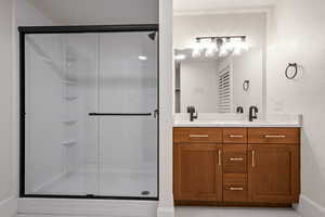 Bathroom featuring double vanity, light tile patterned flooring, a shower stall, and a textured wall