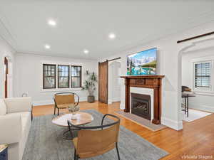 Living area featuring arched walkways, recessed lighting, light wood-style flooring, a glass covered fireplace, and crown molding