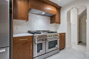 Kitchen featuring stainless steel appliances, light tile patterned flooring, tasteful backsplash, and brown cabinetry