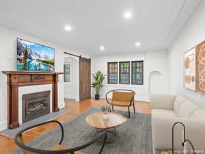 Living room featuring recessed lighting, light wood finished floors, crown molding, arched walkways, and a barn door