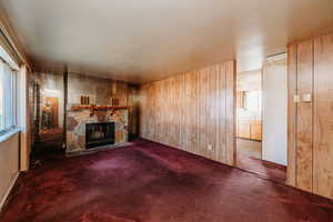 Unfurnished living room with a fireplace, wooden walls, and carpet floors