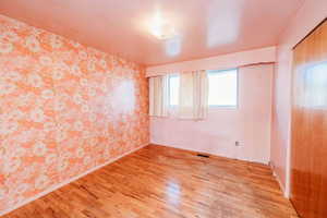 Empty room featuring wallpapered walls, light wood-type flooring, and an accent wall