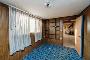 Unfurnished room with wooden walls, a wood stove, built in shelves, and carpet floors