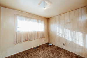 Carpeted spare room featuring wooden walls