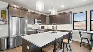 Kitchen with dark brown cabinetry, high end appliances, a breakfast bar area, light wood-style flooring, and a center island with sink