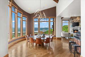 Dining area with vaulted ceiling, a chandelier, a stone fireplace, light wood-style floors, and wallpapered walls
