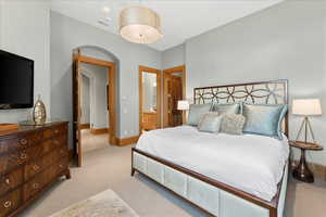 Bedroom with connected bathroom, light colored carpet, and arched walkways