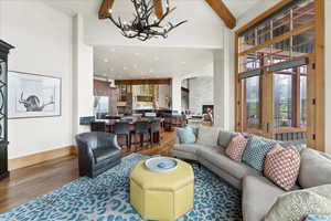 Living room featuring wood finished floors, a high ceiling, a chandelier, beamed ceiling, and a fireplace