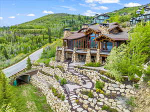 Back of house featuring a chimney, stone siding, a forest view, a patio area, and stairs