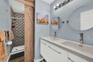 Bathroom with double vanity, a shower stall, and dark wood finished floors