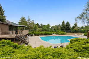 Community pool featuring a wooden deck, a patio, stairway, and view of scattered trees