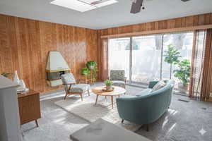 Living area featuring carpet floors, ceiling fan, wood walls, a skylight, and a textured ceiling