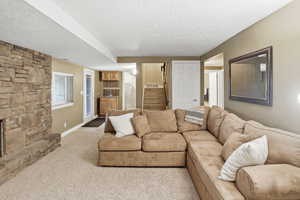 Carpeted living room with stairs, a textured ceiling, and a stone fireplace