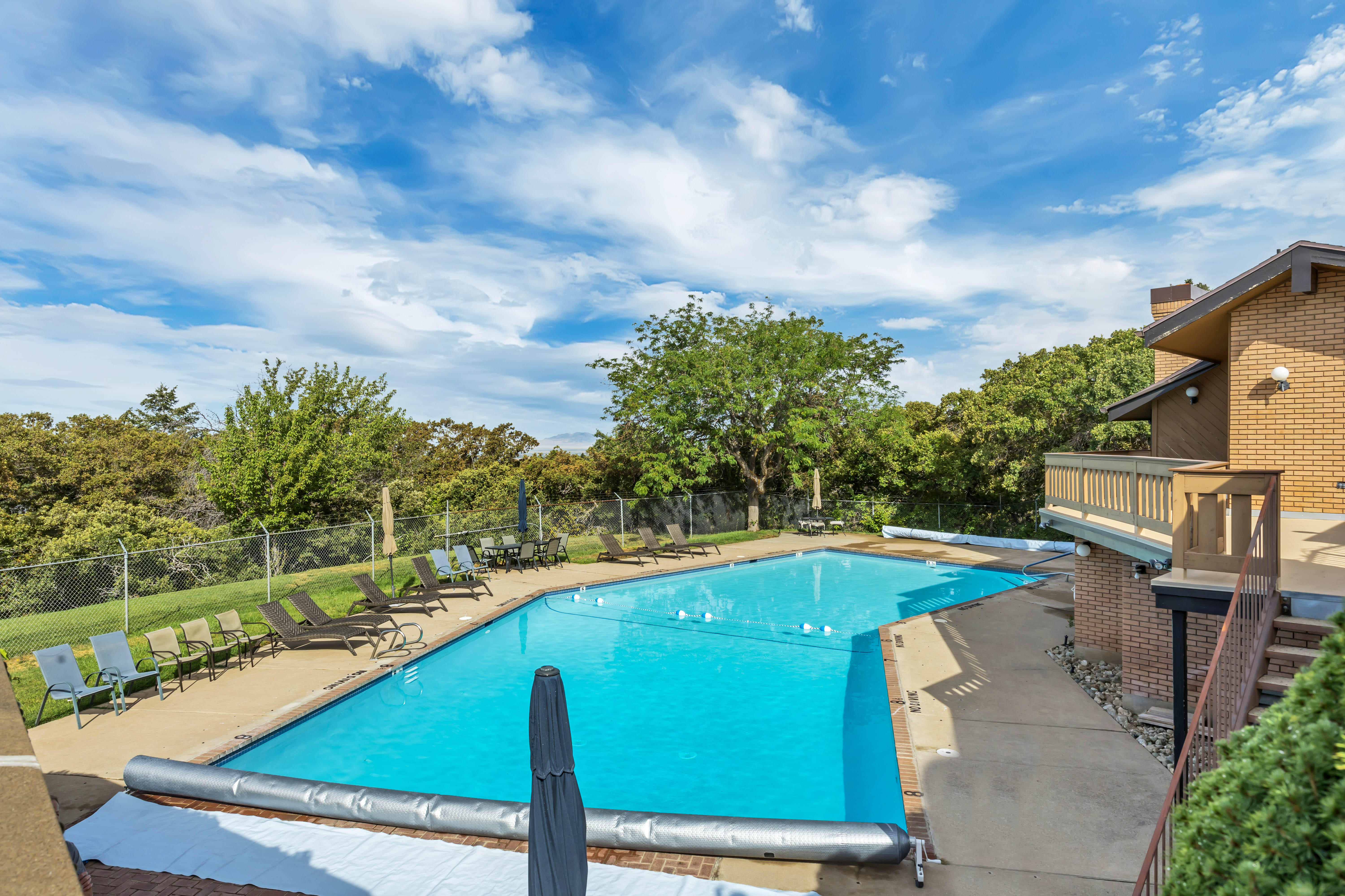 Community pool with a patio and view of wooded area