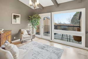 Living area featuring light wood-type flooring, a chandelier, a textured wall, and french doors