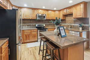 Kitchen with tile counters, a breakfast bar, appliances with stainless steel finishes, a center island, and light wood finished floors