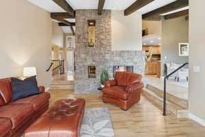 Living area with a stone fireplace, a high ceiling, beamed ceiling, and light wood finished floors