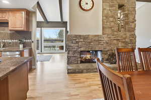 Dining room with beam ceiling, light wood-style flooring, and a stone fireplace