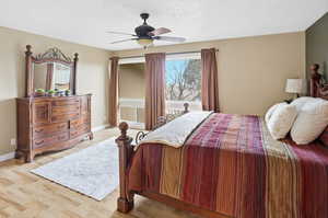 Primary bedroom featuring light wood-type flooring, a textured ceiling, and a ceiling fan