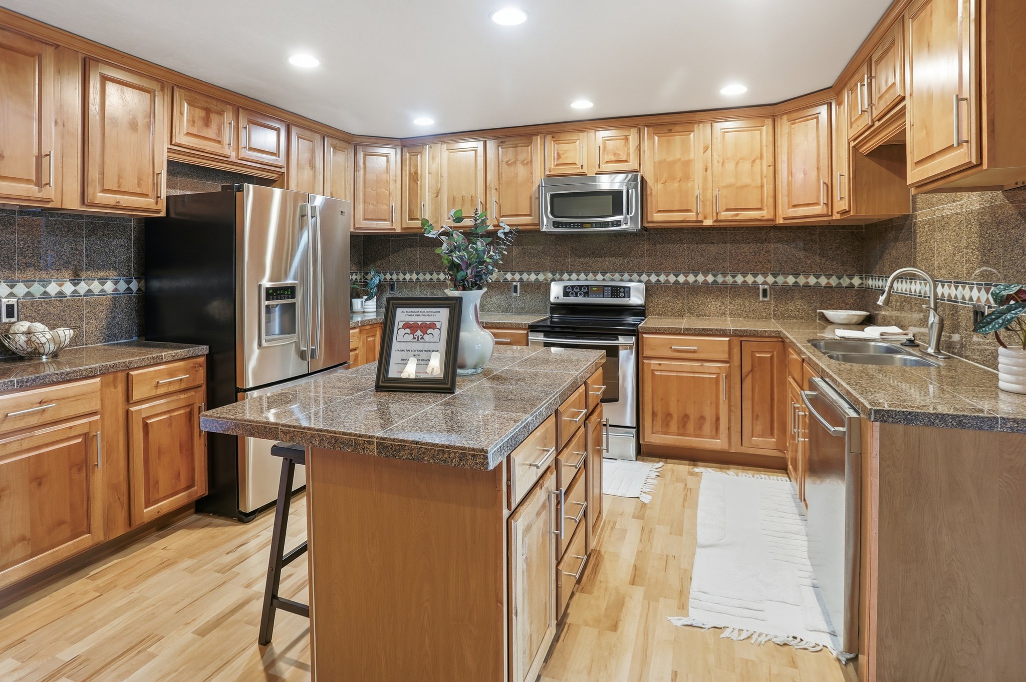 Kitchen with tile counters, a breakfast bar, stainless steel appliances, a kitchen island, and recessed lighting