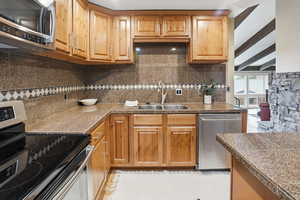 Kitchen featuring tile counters, stainless steel appliances, beamed ceiling, and decorative backsplash
