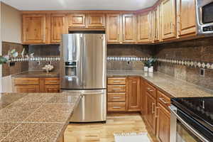 Kitchen with tile countertops, appliances with stainless steel finishes, light wood-style flooring, and brown cabinets