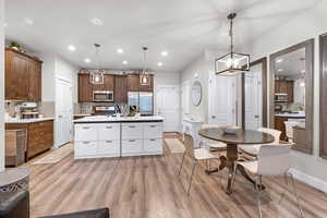 Kitchen featuring backsplash, light wood-style flooring, hanging light fixtures, stainless steel appliances, and an island with sink