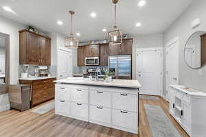 Kitchen with white cabinets, stainless steel appliances, hanging light fixtures, an island with sink, and tasteful backsplash