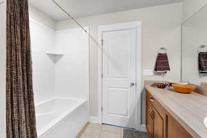 Full bath with shower / tub combo with curtain, vanity, and light tile patterned flooring