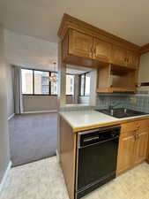Kitchen featuring brown cabinets, light countertops, black dishwasher, brick patterned floors, and a textured ceiling