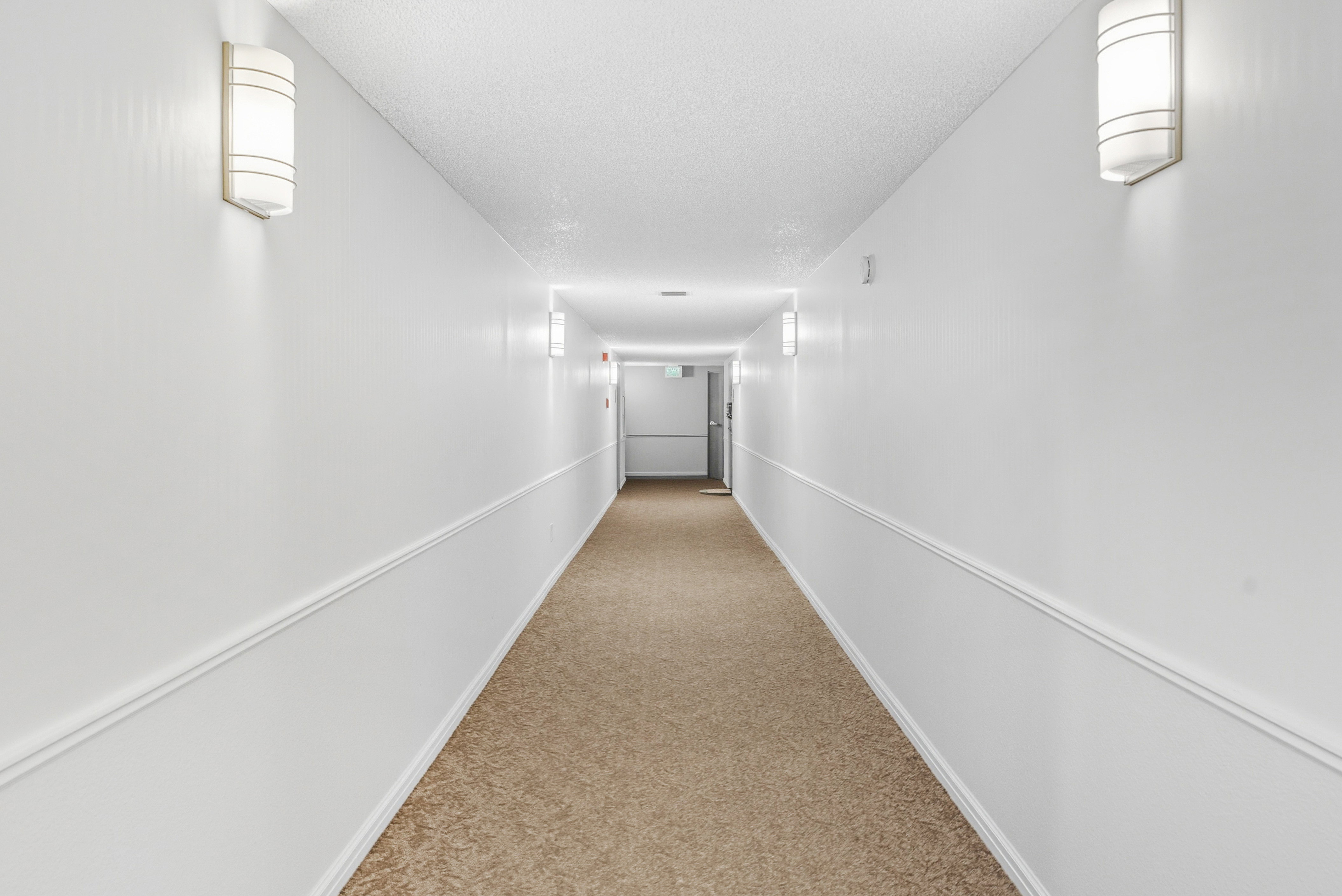 Hallway with light colored carpet and a textured ceiling