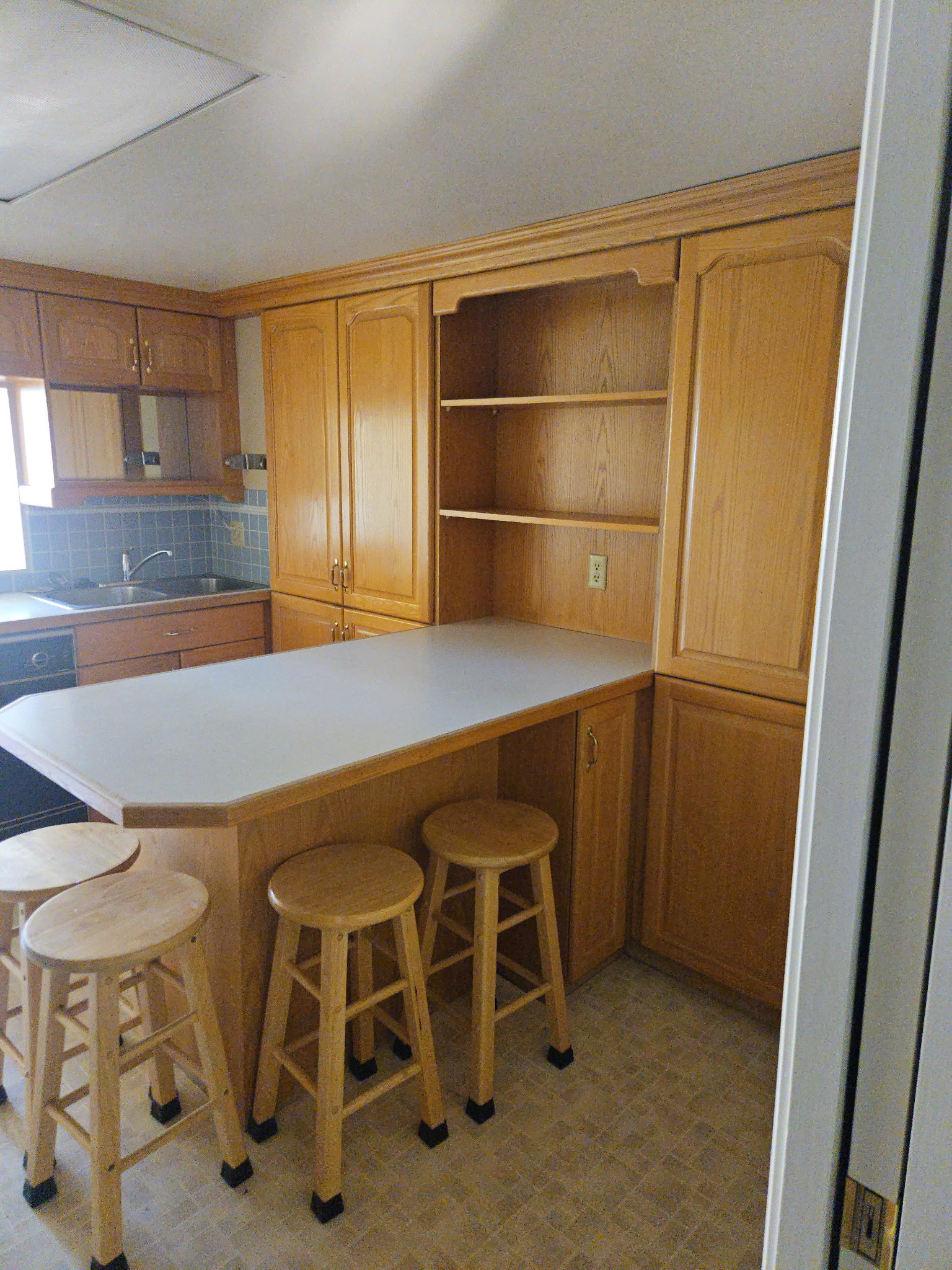 Kitchen featuring open shelves, light countertops, a kitchen breakfast bar, brown cabinets, and backsplash