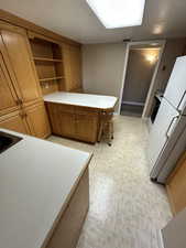 Kitchen with light countertops, brown cabinetry, brick patterned flooring, a peninsula, and freestanding refrigerator