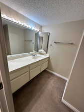 Bathroom featuring vanity, dark carpet, and a textured ceiling