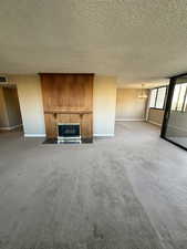 Unfurnished living room featuring carpet flooring, a glass covered fireplace, a textured ceiling, and a chandelier