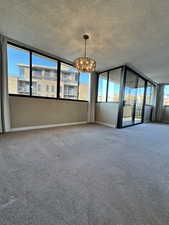 Unfurnished room with a textured ceiling, carpet, healthy amount of natural light, and a chandelier