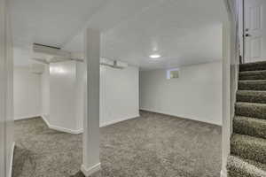 Finished below grade area with a textured ceiling, light colored carpet, and stairs