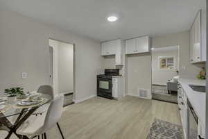 Kitchen featuring black gas stove, white cabinets, light stone counters, light LVP flooring, and dishwasher