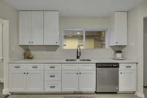 Kitchen with stainless steel dishwasher, white cabinetry, and light stone countertops